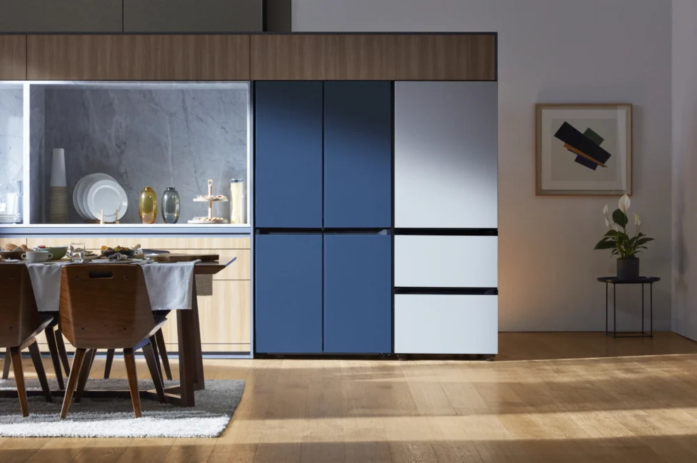 A fitted kitchen in wood and marble with a panelled refrigerator beside a set dining table.