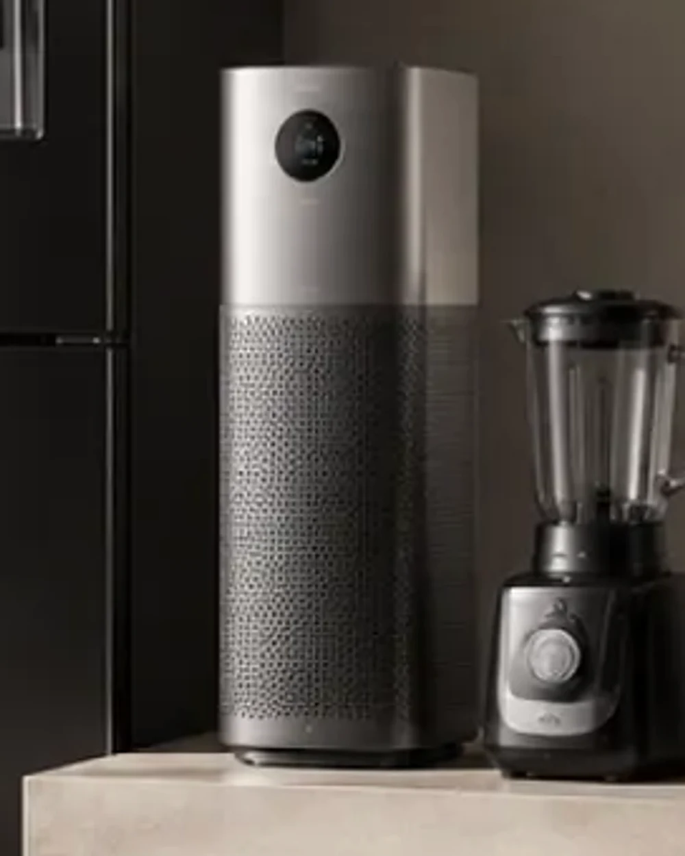 A tower air purifier and a countertop blender beside the flank of a black refrigerator.