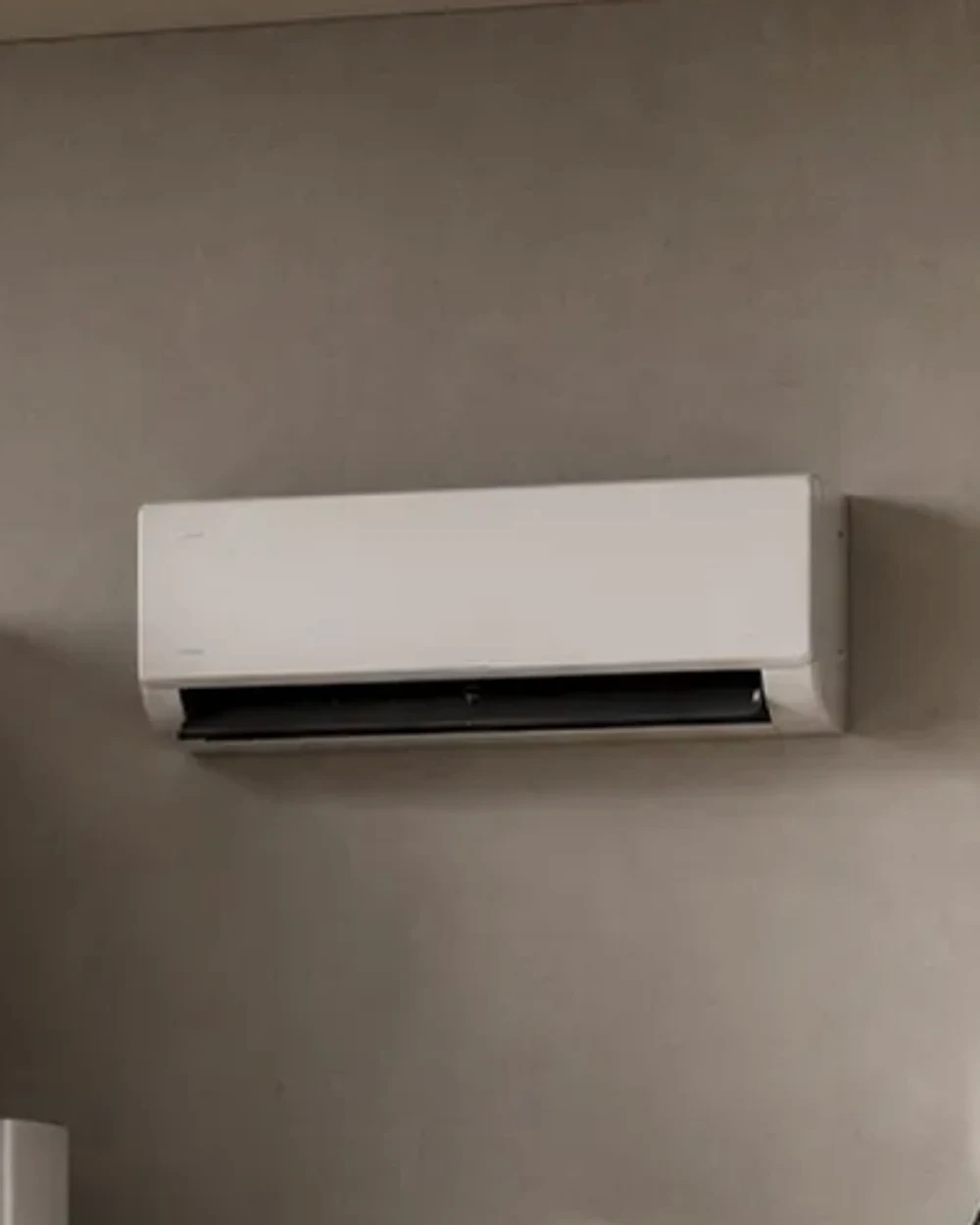 A white wall-mounted split air-conditioning unit on a warm plaster wall.