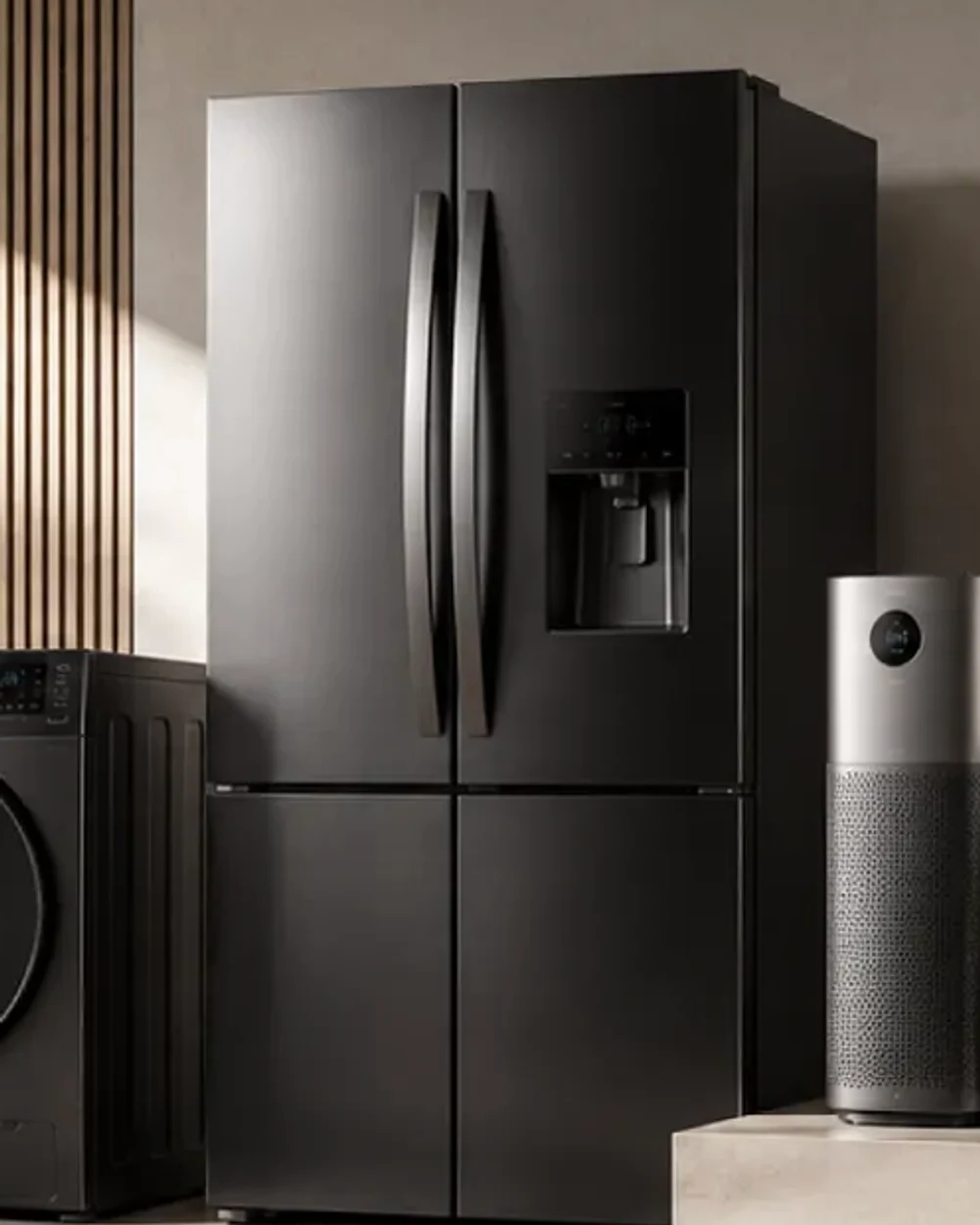A black steel four-door refrigerator with a water dispenser, standing against a pale plaster wall.