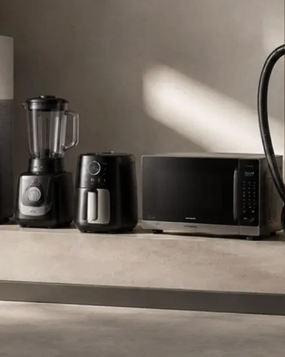 A countertop blender with a glass jug and a dark base, beside an air fryer and a microwave oven.